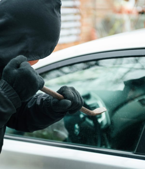 Close-up of a thief wearing balaclava breaking car window with crowbar. Car thief, car theft concept